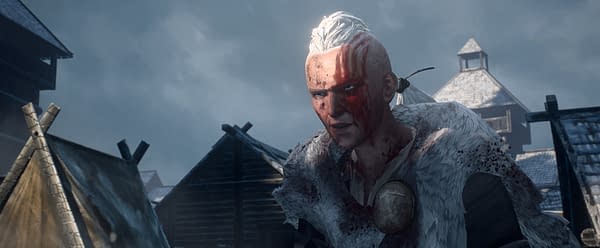 A still from 'PREDATOR: KILLER OF KILLERS' showcasing a character with a fierce expression, bearing blood on their face and traditional clothing, set against a backdrop of dark, cloudy skies and wooden structures. This scene captures the intense atmosphere of the film from 20th Century Studios, streaming exclusively on Hulu.