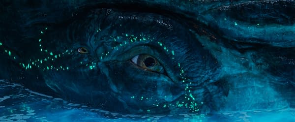 A close-up of Payakan, a prominently featured character with large, expressive eyes and a textured blue-gray skin, illuminated by bioluminescent patterns in water. This image is from 'AVATAR: FIRE AND ASH' by 20th Century Studios.