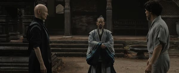 Doctor Strange's Master Hamir stands between two other robed men in a dim temple courtyard scene from Doctor Strange 2.
