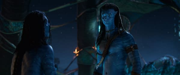 A still from 'Avatar: Fire and Ash' featuring two blue-skinned characters, Lo'ak and Jake Sully, standing close together in a dimly lit environment, showcasing intricate details of their skin patterns and expressions.