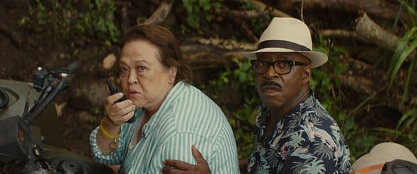 A scene from Disney's live-action 'Lilo & Stitch' featuring Amy Hill as Tūtū, holding a walkie-talkie and looking concerned, alongside Courtney B. Vance as Cobra Bubbles, who appears startled. The background is lush and natural, suggesting a tropical setting.