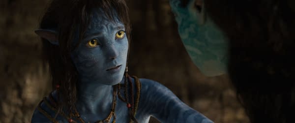 A still from the movie 'AVATAR: FIRE AND ASH,' featuring Kiri, a character portrayed by Sigourney Weaver. She has blue skin adorned with intricate patterns and bright yellow eyes, conveying an emotional expression.