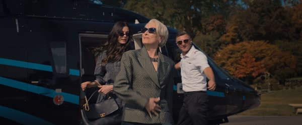 In a scene from 'The Devil Wears Prada 2', Meryl Streep as Miranda Priestly exits a helicopter, dressed in a stylish green striped suit and sunglasses, flanked by Anne Hathaway as Andie Sachs and a crew member. The backdrop features autumn trees in vibrant colors.
