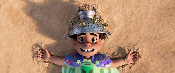 A scene from the animated film 'Elio' featuring a young boy with a cheerful expression lying on sandy ground, wearing a colander as a hat and colorful armor, embracing his imaginative and adventurous spirit. The film, produced by Disney and Pixar, explores themes of space and self-discovery.