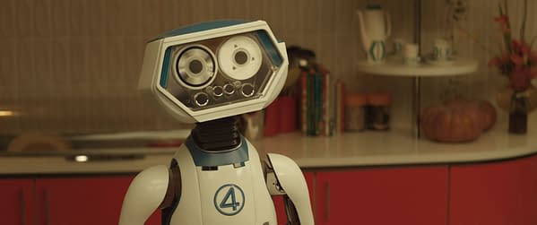 A friendly robot character named H.E.R.B.I.E stands in a modern kitchen setting, featuring a bright red cabinetry and various kitchen items in the background. The design includes a distinctive blue and white color scheme with the number '4' displayed, representing its connection to Marvel's 'The Fantastic Four: First Steps'.