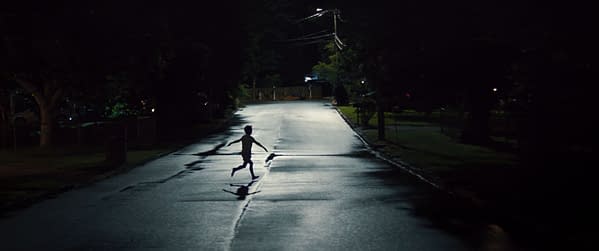 A silhouette of a child running down a dimly lit street at night, with streetlights illuminating the wet pavement.