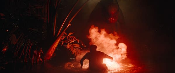 A tense scene from 'Jurassic World Rebirth,' featuring a silhouetted figure in water, illuminated by a glowing object, with a menacing dinosaur emerging in the background, surrounded by dark foliage and smoke.