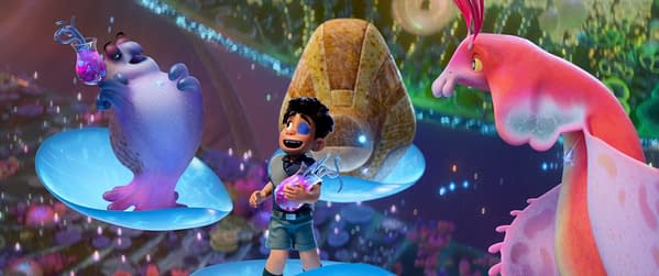 A colorful animated scene from Disney and Pixar's "Elio," featuring the 11-year-old character Elio, who holds a potion while interacting with two unique alien ambassadors. The vibrant, imaginative background showcases an alien landscape filled with fantastical elements.