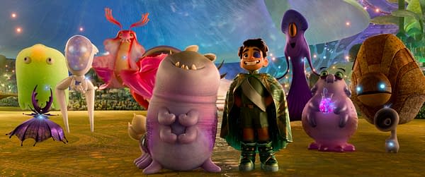 An animated scene from Disney and Pixar's "Elio," featuring the main character Elio, a young boy in a green cape, standing among colorful alien creatures, including Glordon, an oversized purple character, and several other whimsical aliens representing various galaxies.