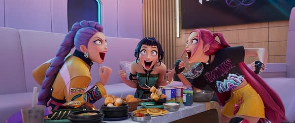 Animated scene from 'KPOP DEMON HUNTERS' featuring three characters—Rumi, Zoey, and Mira—expressing excitement while surrounded by an array of food on a table. The setting appears colorful and vibrant, showcasing a dynamic and fun atmosphere.