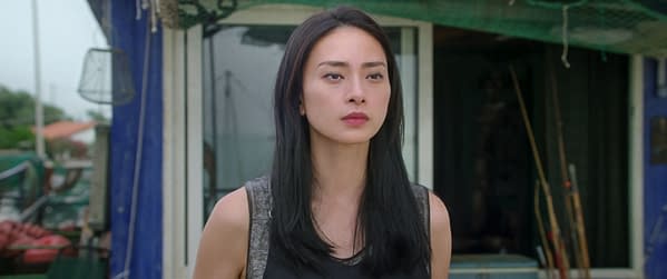 Veronica Ngô portrays Quynh in The Old Guard 2, standing outside a building with a contemplative expression, her long black hair cascading over her shoulders.
