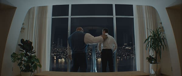 A scene from 'The Fantastic Four: First Steps' featuring Ebon Moss-Bachrach as Ben Grimm/The Thing and Pedro Pascal as Reed Richards/Mister Fantastic. They stand side by side looking out a large window at a city skyline at night.