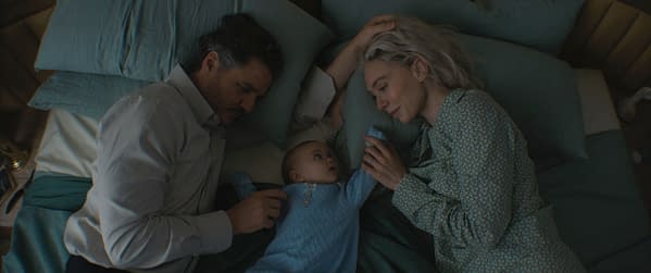 A scene from 'The Fantastic Four: First Steps' featuring characters Reed Richards, played by Pedro Pascal, and Sue Storm, played by Vanessa Kirby, lying on a bed with their baby Franklin Richards. The trio is surrounded by soft pillows and blankets, creating an intimate family moment.