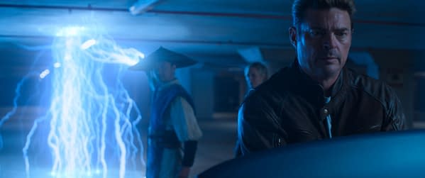A dramatic scene from Mortal Kombat II, featuring a character in a leather jacket looking intently at a glowing blue lightning effect, while another character in a traditional outfit and hat stands behind him.