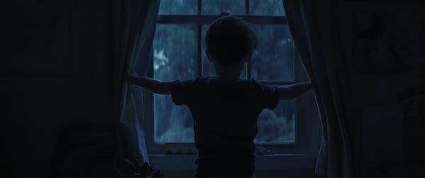 A silhouette of a child standing at a window, pulling back the curtains in a dimly lit room, suggesting a sense of curiosity or apprehension. The scene has a moody blue tint, enhancing the atmosphere.