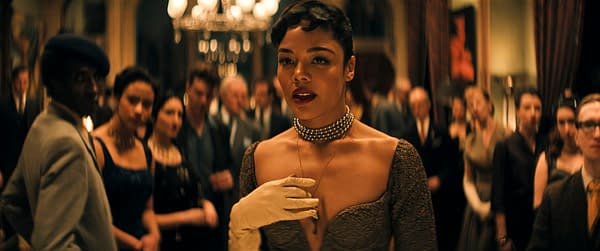 Tessa Thompson portrays Hedda Gabler in a stylish scene set in a crowded event, highlighting classic fashion and vintage ambiance.