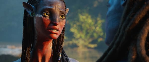 A character named Neytiri, portrayed by Zoe Saldaña in 20th Century Studios' 'AVATAR: FIRE AND ASH', is depicted with intricate facial markings and braided hair, expressing a strong emotion against a lush backdrop.