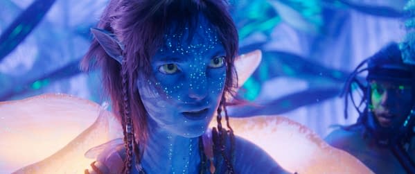 A close-up of Kiri, portrayed by Sigourney Weaver, from 'AVATAR: FIRE AND ASH,' showcasing her blue skin adorned with luminous patterns against a vibrant, mystical background. Her expression conveys a sense of intensity and connection to her surroundings.