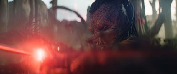 A character named Dek, portrayed by Dimitrius Schuster-Koloamatangi, is depicted in a dynamic pose in a scene from 20th Century Studios' film "Predator: Badlands," showcasing a menacing expression amidst a dramatic red light.