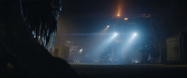 A scene from the film 'PREDATOR: BADLANDS' depicting a menacing creature observing a military-like vehicle illuminated by bright lights in a dark setting.