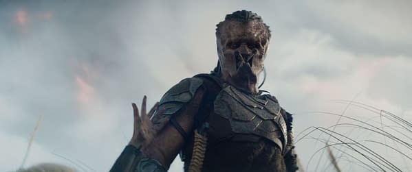 Dimitrius Schuster-Koloamatangi as Dek in 20th Century Studios' 'Predator: Badlands,' featuring a menacing character in a rugged costume with a distinctive facial appearance set against a dramatic sky.
