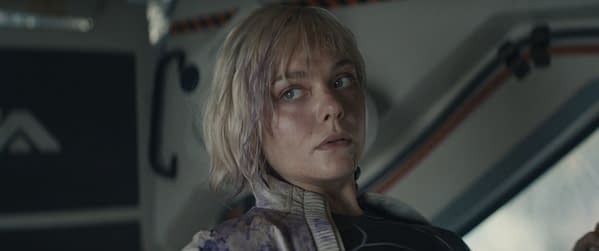A close-up of Elle Fanning as Thia from the film 'Predator: Badlands,' showcasing her intense expression and disheveled look, suggesting a tense atmospheric moment.