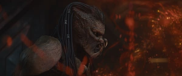 A close-up of the character Kwei, portrayed by Mike Homik, from the film 'Predator: Badlands' by 20th Century Studios, featuring a fierce expression and detailed features in a dramatic, shadowy setting.