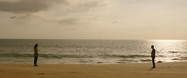 A scene from the film 'SEND HELP' featuring Rachal McAdams as Linda Liddle and Dylan O'Brien as Bradley Preston, standing apart on a sandy beach with the ocean in the background under a cloudy sky.