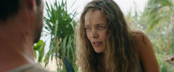 Rachel McAdams, portraying Linda Liddle, has an intense expression as she interacts with another character in a scene from 20th Century Studios' 'SEND HELP'. Tropical plants are visible in the background, adding to the dramatic atmosphere.