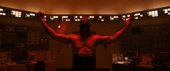 A dramatic scene featuring James Preston Rogers portraying a character called Psycho Killer, with bare arms raised and a gas mask, set in a dimly lit control room adorned with blinking lights.