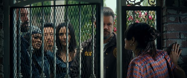 A scene from 'The Rip' featuring a group of detectives, including characters portrayed by Ben Affleck and Teyana Taylor, looking through a barred gate at a woman on the other side. The setting suggests a tense or dramatic interaction.