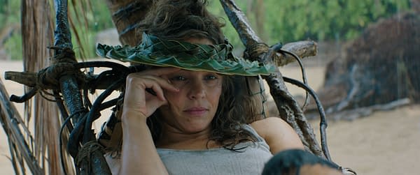 Rachel McAdams as Linda Liddle, wearing a woven leaf hat and looking contemplative, in a scene from the movie 'Send Help.' The background features a natural, tropical setting.