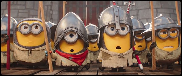 A group of Minions dressed as medieval soldiers, wearing helmets and tattered clothing, stand in formation. One Minion in the front holds a spear and wears a red bandana, looking curious.