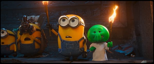 Two Minions and a green monster character holding torches, set in a dark cave with ancient markings in the background. They appear to be in a state of excitement or surprise.