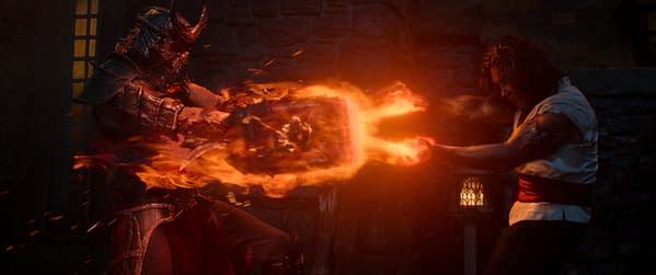 A dramatic scene from Mortal Kombat II, featuring two characters in combat. One character, wearing a fearsome armor with a helmet and holding a flaming weapon, displays intense energy as it clashes with the other character, who is casting a fiery spell. The background includes a dimly lit stone structure.