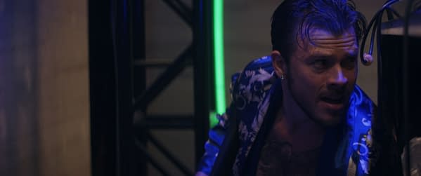 A scene from the film 'Mike & Nick & Nick & Alice' featuring Jimmy Tatro as his character, Jimmy Boy, looking intense while dressed in a floral-patterned shirt. The backdrop has dramatic lighting with a hint of neon green.