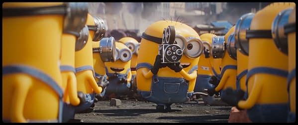 Minions in denim overalls crowd around a central Minion holding a vintage movie camera, from Illumination's Minions & Monsters.