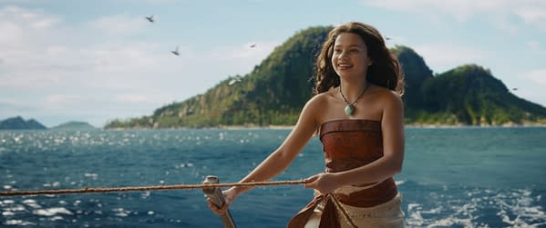 Catherine Laga'aia as Moana smiles while steering a boat across the ocean in Disney's live-action Moana, with tropical islands in the background.