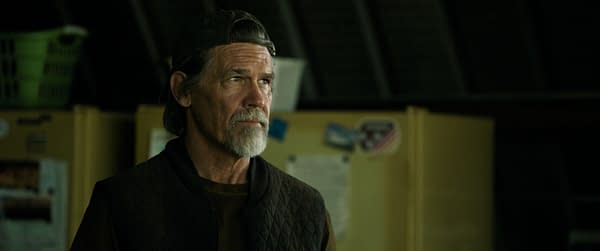 Josh Brolin as Bangley stands in a dimly lit room in The Dog Stars, wearing a backward cap and looking off to the side.