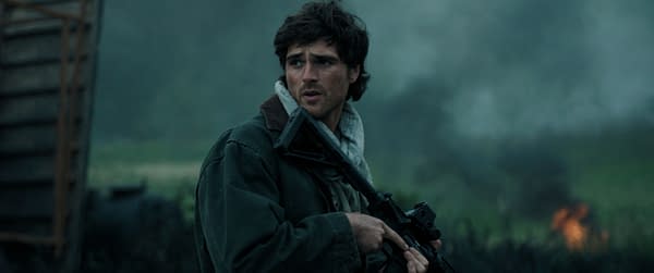 Jacob Elordi as Hig stands alert with a rifle in a tense, smoky outdoor scene from The Dog Stars.
