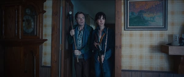 A tense scene from The End of Oak Street Review shows two people cautiously entering a dimly lit room, each holding a long gun or rifle.