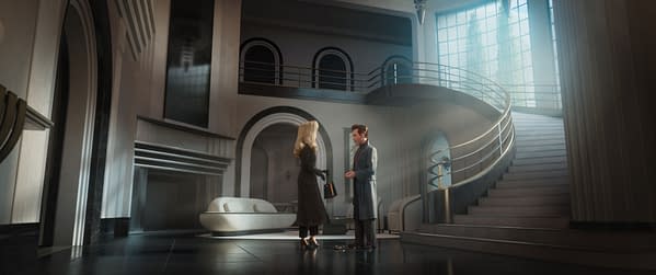 Venus Nova and Raymond Gunn stand talking in a sleek Art Deco-style mansion with a sweeping staircase and bright skylight in Ray Gunn.