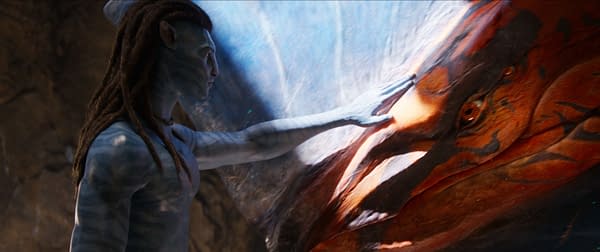 A still from the movie 'Avatar: Fire and Ash' featuring Jake Sully, a blue-skinned character, gently touching a colorful, dragon-like creature. The scene captures a moment of connection between the character and the mystical being.