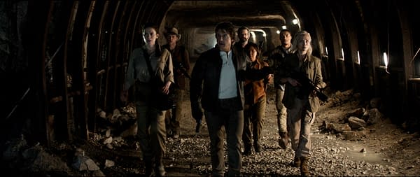 A scene from 'Mission: Impossible - The Final Reckoning' featuring a group of seven characters walking through a dimly lit underground passage, dressed in tactical gear and appearing focused and alert.