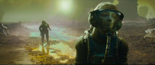 A scene from 'Rogue Trooper' featuring two astronauts in a desolate, alien landscape with surreal colors and textures. One astronaut, in the foreground, is looking intently, while another explores in the background.