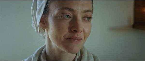 Close-up of a woman with soft features and green eyes, wearing a white headscarf and a light-colored outfit, portraying a character from 'The Testament of Ann Lee'.