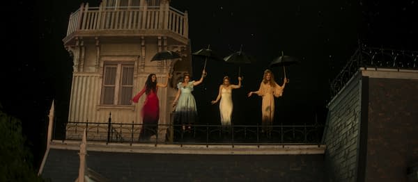 Four women in flowing dresses hold umbrellas while standing on a rooftop balcony at night in a Practical Magic 2 scene.