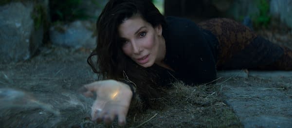 A woman with long dark hair lies on the ground, reaching out with her hand as if casting a spell or summoning magic. The background is dimly lit, creating an ethereal atmosphere.