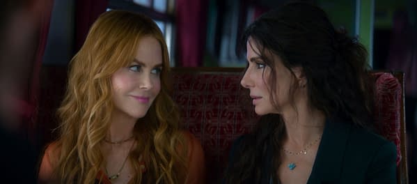 A scene from 'Practical Magic 2' features two women seated side by side, exchanging knowing glances. One woman has long, wavy blonde hair, while the other has dark, wavy hair, both adorned with delicate jewelry.