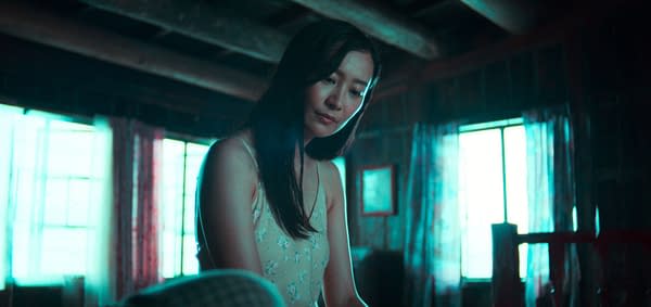 Ballad of a Small Player A woman with long dark hair sits thoughtfully in a room with wooden beams and blue-tinted light coming through windows, wearing a light floral dress.